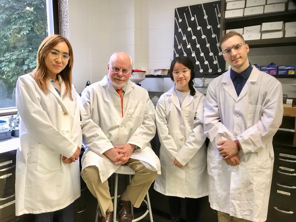 four students in lab coats standing in a lab